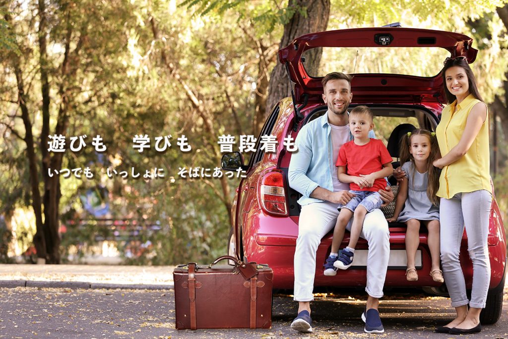 家族4人が車の前で旅をする様子。手前には革のトランク。「遊びも　学びも　普段着も」「いつでも　いっしょに　そばにあった」の文字